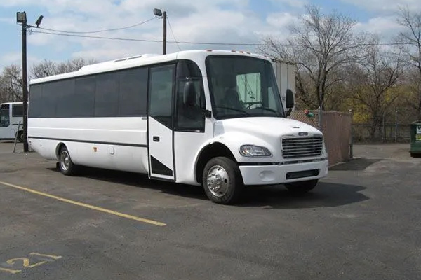 A white bus parked next to a fence in a city street